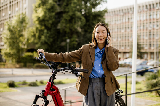 Woman talks on phone while standing next to electric bike in urban area