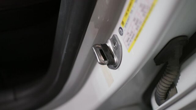 Car door latch striker plate mounts firmly on the white vehicle pillar frame. Soft diffused ambient lighting reveals the metallic surface and automotive interior door jamb.