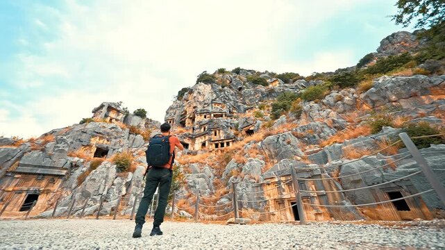 Myra Ancient City in Demre, Antalya, Turkiye, shows a photographer walking and capturing the majestic Lycian rock tombs with his camera.