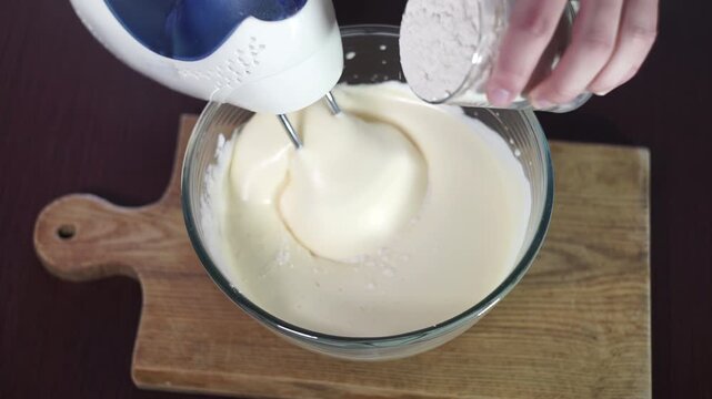 Pouring flour creamy batter glass bowl close up. Mixer whipping dough overhead.
