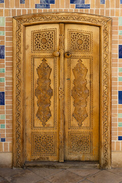 Ornate carved wooden door with geometric Islamic patterns at Hazrat Khizr mosque in Samarkand. Traditional Uzbek woodcarving craftsmanship set in a colorful tiled brick wall, ideal for travel.