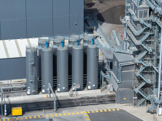 Row of tall cylindrical grey storage silos connected by overhead piping and access platforms next to an asphalt production tower at an industrial road materials facility in western Sydney © Paul Tama