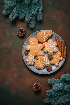Christmas gingerbread cookies on a plate and decorative spruce branches on a dark rustic background, top view, flat lay, copy space, vertical