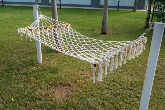 White woven rope hammock hanging on posts over a green grass lawn in a garden