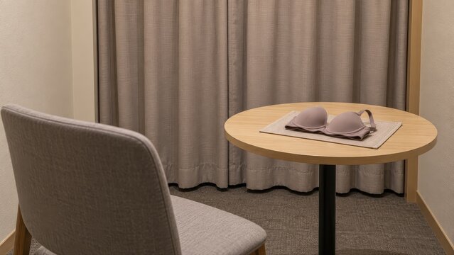 Folded everyday bra rests on its own fabric mat beside an empty chair and closed curtain in a private retail consultation alcove prepared for a fitting appointment