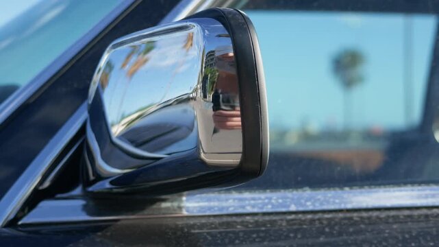 Close-up of a chrome side mirror on a dark vintage car reflecting palm trees and a blue sky, French Riviera, France.