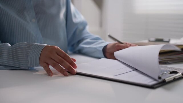 Office employee arranging printed financial paperwork in a folder at a desk, representing business document organization, accounting administration, bookkeeping, and professional record management.
