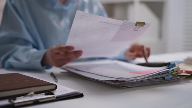 Office worker holding and reviewing printed financial documents beside a calculator, illustrating accounting review, expense analysis, bookkeeping, budget planning, and business paperwork management.