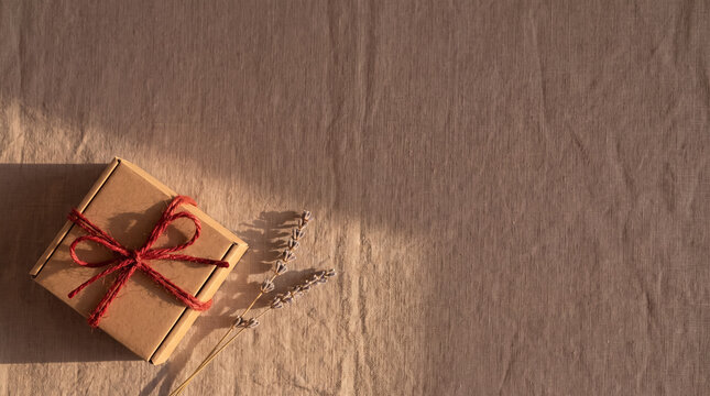 Crafting a sustainable gift, brown cardboard box with red string bow and lavender on linen fabric, bathed in warm sunlight