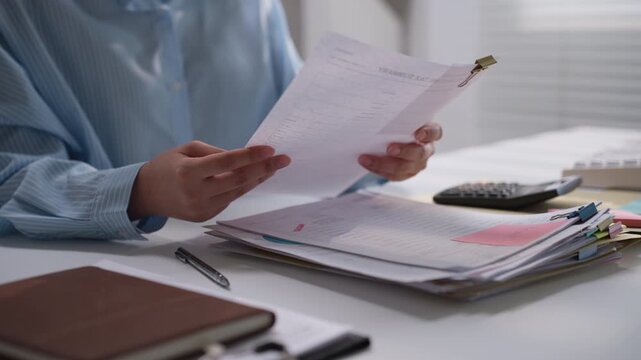Office professional reviewing financial statements above organized paperwork, representing accounting verification, financial analysis, document processing, and routine business administration.