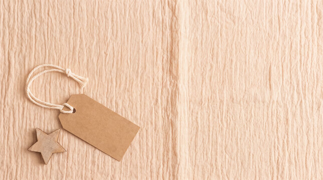 Blank brown cardboard tag with string and wooden star, offering copy space on textured fabric background