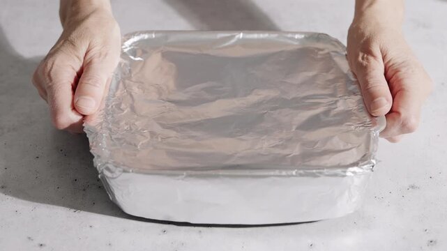 Hands Hold A Baking Tray Covered With Aluminum Foil.