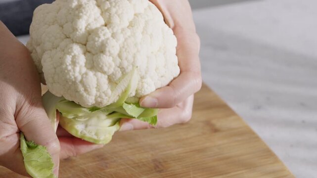 Hands Remove Green Leaves From Fresh Cauliflower On A Wooden Board.