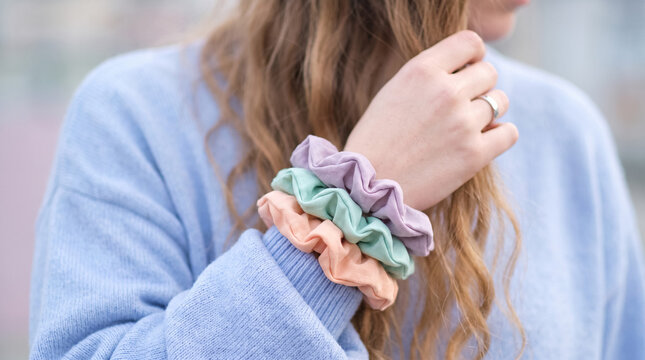 Woman's arm with scrunchies on the wrist, pastel colors. Capturing a cozy fashion trend and personal style