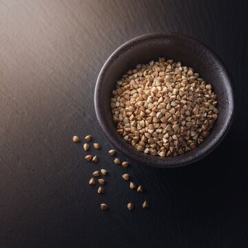Raw buckwheat groats in a dark ceramic bowl with scattered grains