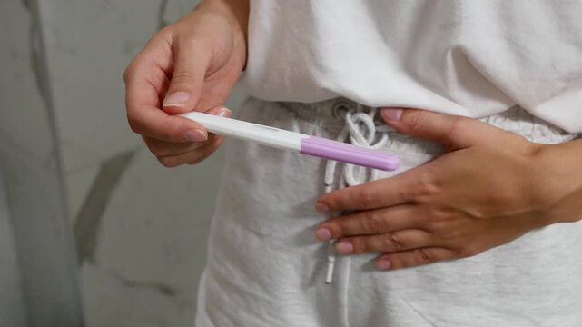 Close-up of woman holding pregnancy test and touching belly, concept of pregnancy planning and reproductive health