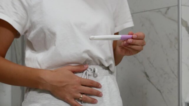 Close-up of woman holding pregnancy test and touching her belly, pregnancy concerns and reproductive health concept