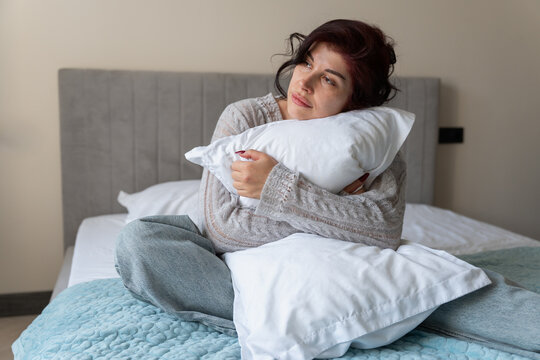 Woman relaxing in bed while hugging a pillow at home
