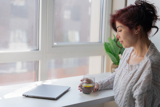 Woman relaxes with lemon water beside laptop at home