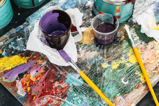 Colorful paint palette with brush and cup in art studio