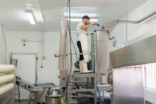 Dairy worker operating stainless steel milk processing equipment