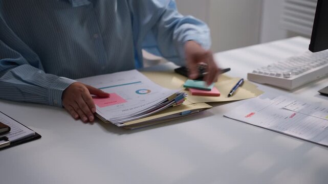 Business professional reviewing a stack of financial reports with colorful document tabs and a calculator nearby, illustrating accounting accuracy, bookkeeping, and administrative record management.