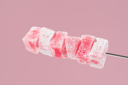 Pink Turkish delight cubes on a skewer against pastel background