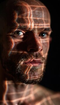 Man with luminous geometric lines projected on face in dark studio