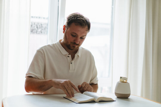 Man reading Bible with tea at home by window