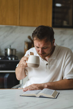 Man reading Bible and drinking tea at kitchen table
