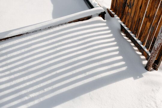 Snow-covered wooden fence with winter sunlight and shadow
