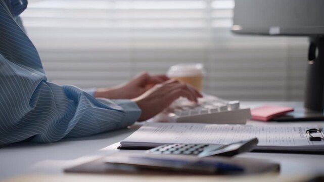 Business professional using a white computer keyboard at a desk with financial paperwork, illustrating accounting data entry, electronic record management, office productivity, and bookkeeping workflo