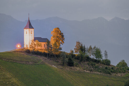 Illuminated church on slovenian hill beneath mountain range