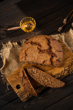 Rustic dark rye bread loaf with honey on wooden board