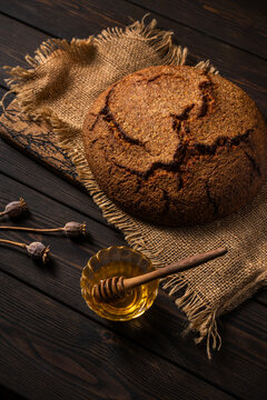 Rustic dark rye bread loaf with honey on wooden table