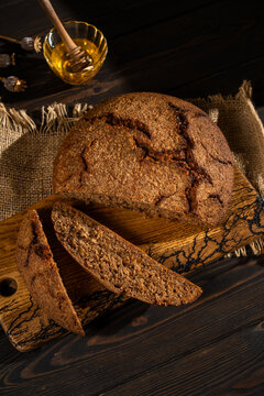 Rustic dark rye bread loaf with honey on wooden table