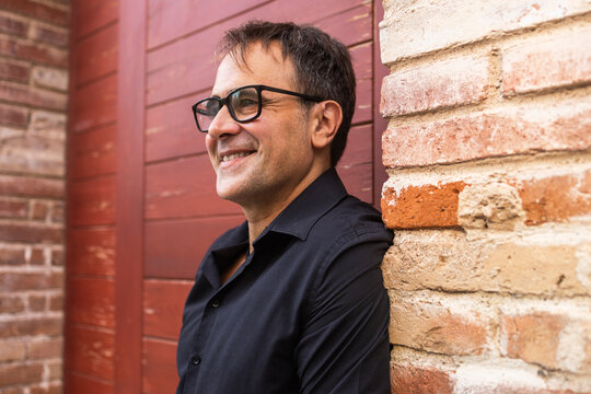 Smiling mature man in glasses leaning against brick wall