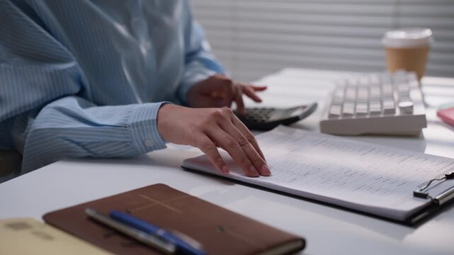 Business professional reviewing printed accounting paperwork beside a notebook and computer keyboard, illustrating financial record checking, bookkeeping accuracy, and organized office administration.