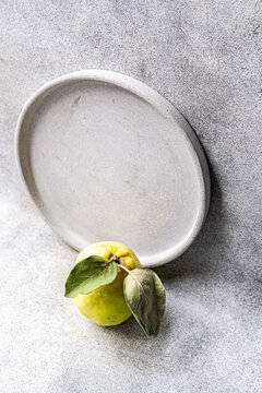 Ripe quince with leaf beside empty ceramic plate