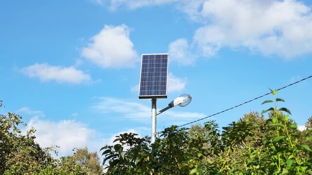 Solar powered street lamp on a metal pole above green bushes under a blue sky.
