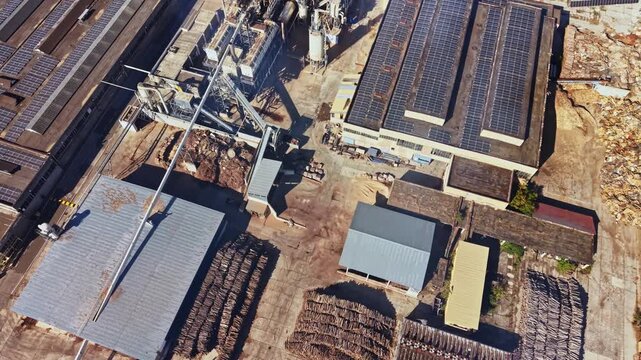 An aerial view shows machinery and rows of stacked materials at an industrial recycling facility, with solar panels on the roofs under daylight.