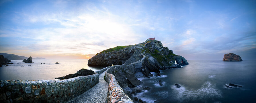 Wide panorama of the cobbled bridge and stairway to the islet of San Juan de Gaztelugatxe at blue hour with silky Cantabrian waves