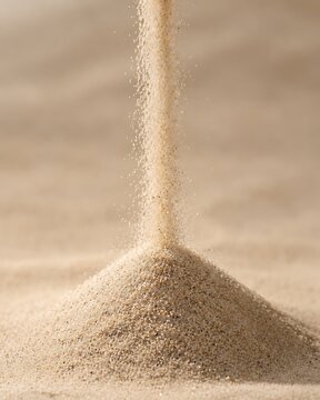 Fine grains of sand cascade down, forming a small mound on a sandy surface, emphasizing texture and movement.