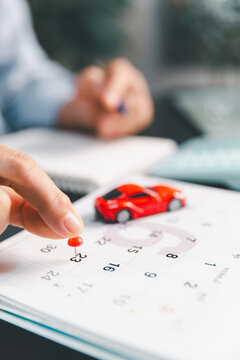 Close-up of a hand pinning a calendar date beside a model car, symbolizing car payment deadlines, loan scheduling, monthly budgeting, purchase planning and vehicle finance for expense control.