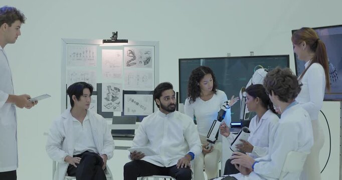 The team sits in a close circle around the robotic arm prototype, handling the gripper and a grip test ball while an engineer takes notes on a tablet behind them.