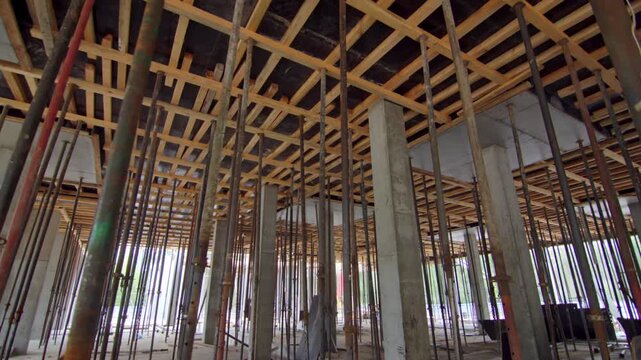 Steel shoring poles extend upward to reinforce ceiling beam mold. Raw industrial setting reflects active floor pouring preparation
