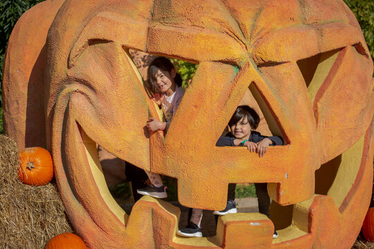 Children peeking through a giant Halloween pumpkin decoration