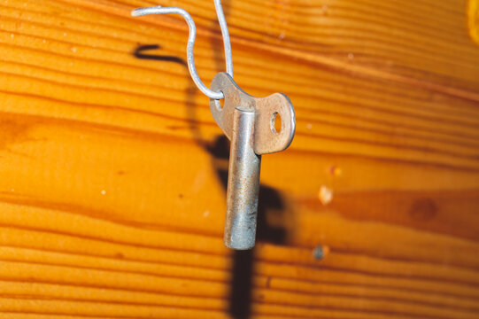 T-shaped metal wrench hanging with a light wooden board background