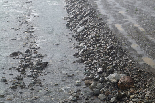 Rocky river bank with puddles and fast water in the rain