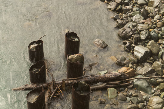 Rusty metal pipes in river next to rocky bank in the rain